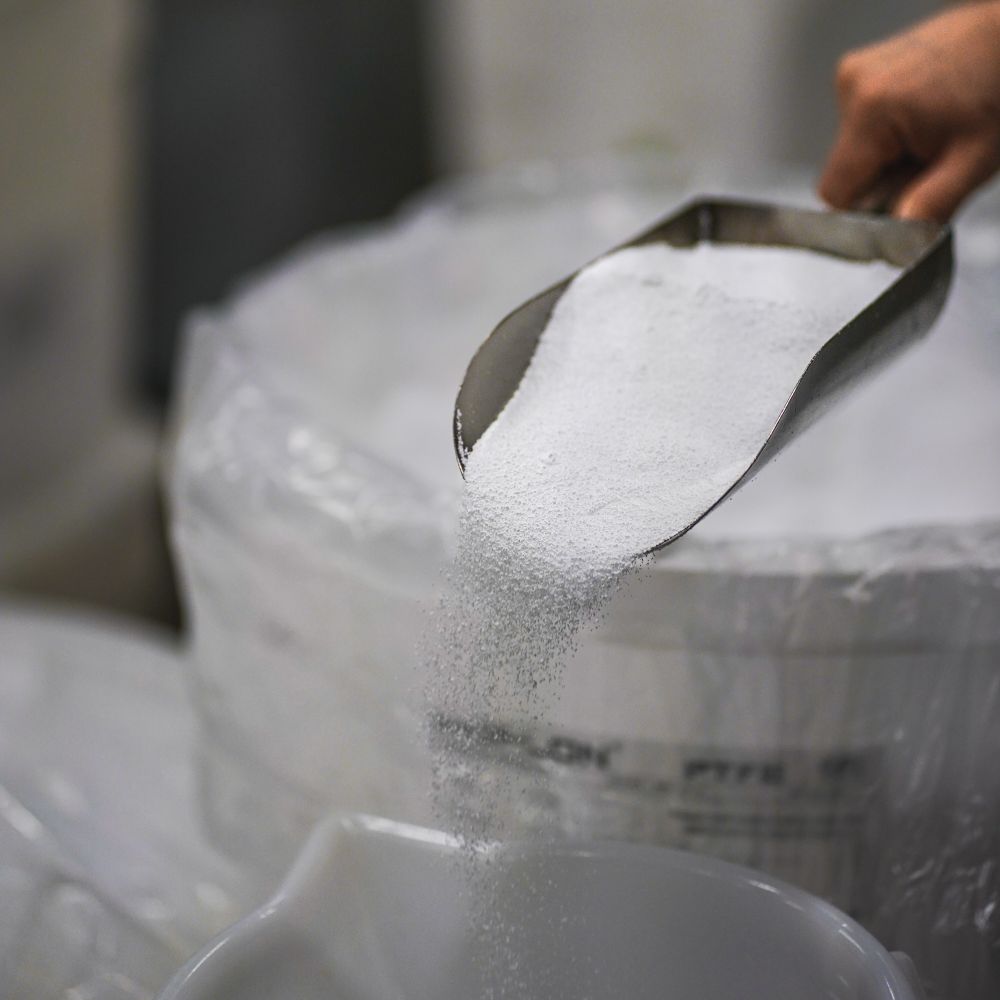 Hand hält eine Schaufel mit weißem PTFE Granulat