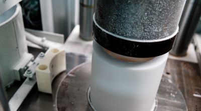 Pieza cilíndrica blanca de PTFE en una prensa, compactada desde arriba con un punzón metálico