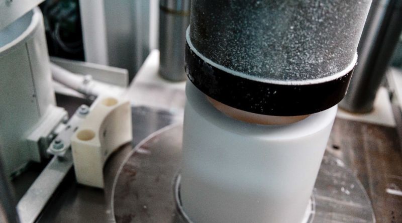 Pieza cilíndrica blanca de PTFE en una prensa, compactada desde arriba con un punzón metálico